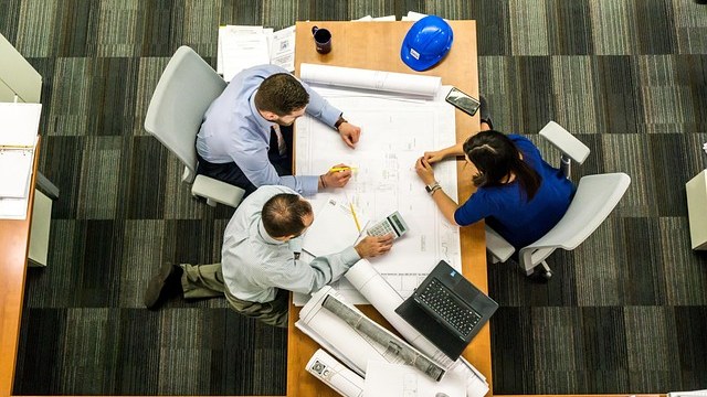 Tres personas trabajando sobre unos planos en una mesa, vistas desde arriba
