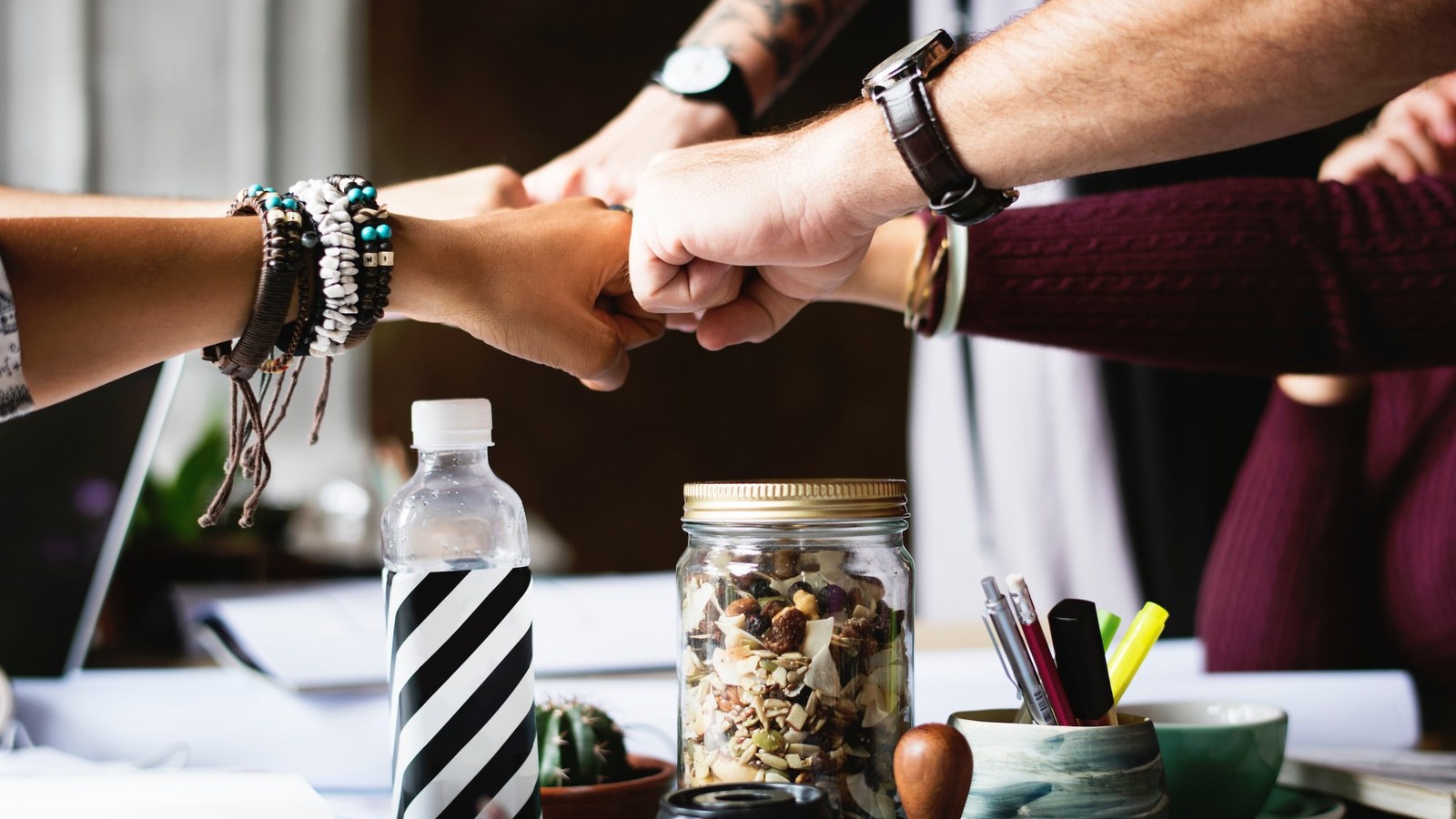 Varias manos de un equipo chocando los puños sobre una mesa de trabajo
